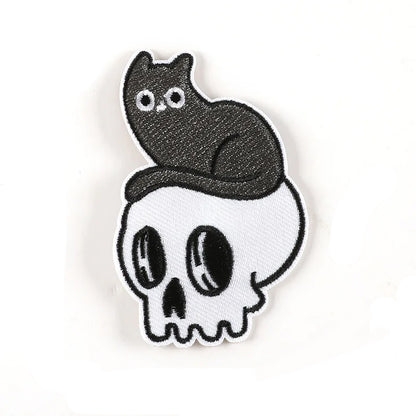 Brodert strykemerke av katt som sitter oppå en hodeskalle